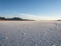 a lone desert area in a deserted area with the sky and mountains behind it with footprints in the sand