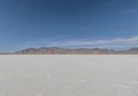 a lone motorcycle is on a deserted plain in the desert with some mountains behind it