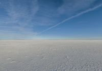 a lone person walking in an open area on top of snow covered ground under a blue sky