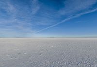 a lone person walking in an open area on top of snow covered ground under a blue sky