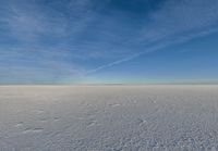 a lone person walking in an open area on top of snow covered ground under a blue sky