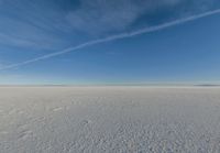 a lone person walking in an open area on top of snow covered ground under a blue sky