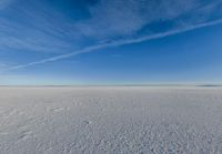 a lone person walking in an open area on top of snow covered ground under a blue sky