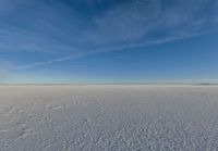 a lone person walking in an open area on top of snow covered ground under a blue sky