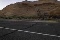 a lone road near the desert mountains with the moon in the sky behind it,