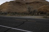 a lone road near the desert mountains with the moon in the sky behind it,