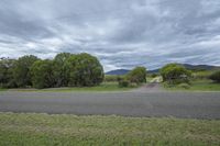 a lone road is near some trees and a field with mountains in the background at dusk