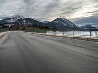 a lone skateboarder is traveling across the bridge near snow - capped mountains near an empty road