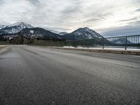 a lone skateboarder is traveling across the bridge near snow - capped mountains near an empty road