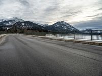 a lone skateboarder is traveling across the bridge near snow - capped mountains near an empty road