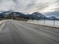 a lone skateboarder is traveling across the bridge near snow - capped mountains near an empty road