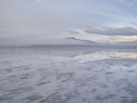 a lonely beach with cloudy skies in the distance, reflecting water on the sand and a building on the shore of the other side