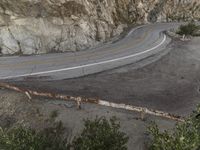 a bird eye view of a lonely curve in the country road with mountain side cliffs behind it