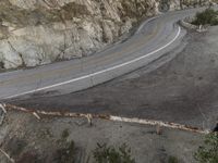 a bird eye view of a lonely curve in the country road with mountain side cliffs behind it