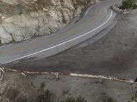 a bird eye view of a lonely curve in the country road with mountain side cliffs behind it