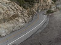 a bird eye view of a lonely curve in the country road with mountain side cliffs behind it