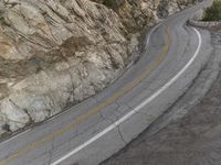 a bird eye view of a lonely curve in the country road with mountain side cliffs behind it