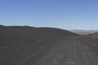 a lonely dirt road in the middle of an arid area with mountains in the distance