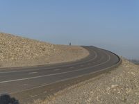 there is a lone road by some mountains in the desert in the afternoon light from behind