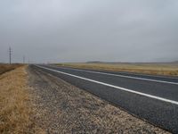 a lonely road winds across the open desert area on an overcast day in the far distance, a single line of telephone poles are present