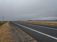 a lonely road winds across the open desert area on an overcast day in the far distance, a single line of telephone poles are present