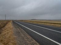 a lonely road winds across the open desert area on an overcast day in the far distance, a single line of telephone poles are present