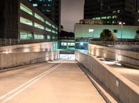 an empty walkway with buildings and lights shining brightly in the background and also a white dotted road