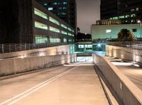 an empty walkway with buildings and lights shining brightly in the background and also a white dotted road