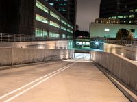 an empty walkway with buildings and lights shining brightly in the background and also a white dotted road