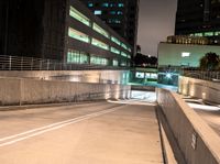 an empty walkway with buildings and lights shining brightly in the background and also a white dotted road