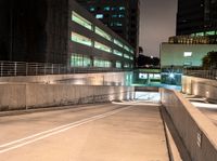 an empty walkway with buildings and lights shining brightly in the background and also a white dotted road