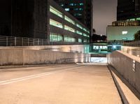 an empty walkway with buildings and lights shining brightly in the background and also a white dotted road