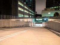 an empty walkway with buildings and lights shining brightly in the background and also a white dotted road