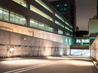 an empty walkway with buildings and lights shining brightly in the background and also a white dotted road