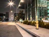 a yellow fire hydrant is located by the street at night on a sidewalk near a tall building