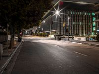 a empty street in front of some tall buildings at night time with street lights and cars passing by