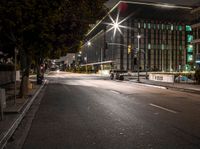 a empty street in front of some tall buildings at night time with street lights and cars passing by