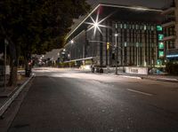 a empty street in front of some tall buildings at night time with street lights and cars passing by