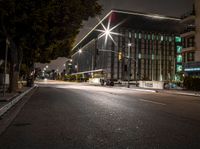 a empty street in front of some tall buildings at night time with street lights and cars passing by