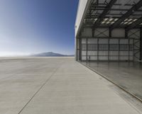 a very long cement runway near an airplane hangar with mountain in background and blue sky