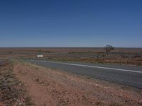 a long empty road stretches along a wide plain and it is paved with a white sign