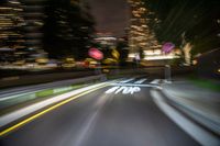 motion blurry shot of a long road at night with a traffic signal and city skyline in the background