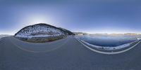 a long road with mountains in the background with ice, on the horizon and water below