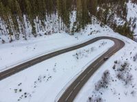 a long and winding road with vehicles driving through the snow in front of a forest