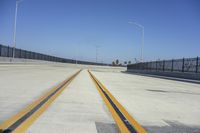 a long yellow line on a deserted road next to traffic light poles and fenced off area