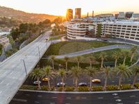 an intersection with cars and palm trees in the sunset with a light on each side