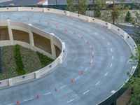 an aerial view of a curve road near trees and buildings with traffic cones in front of it