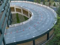 an aerial view of a curve road near trees and buildings with traffic cones in front of it