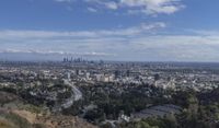 a view from a hill overlooking a city and some hills, and trees on either side of the city