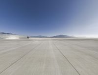 an empty cement runway with hills behind it in the distance is sky filled with cloudless clouds